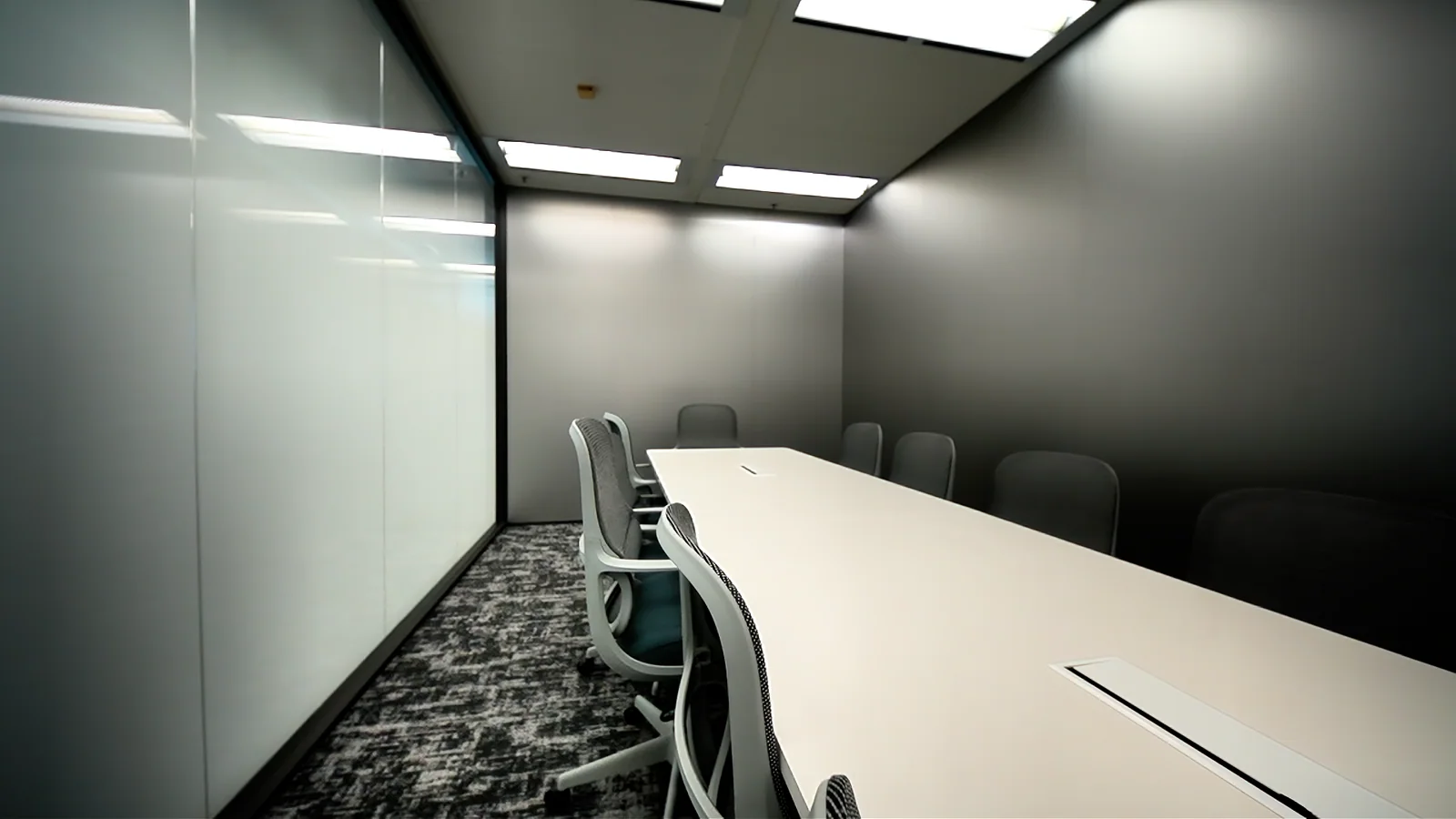 Long white meeting table and grey chairs beside a frosted glass partition.