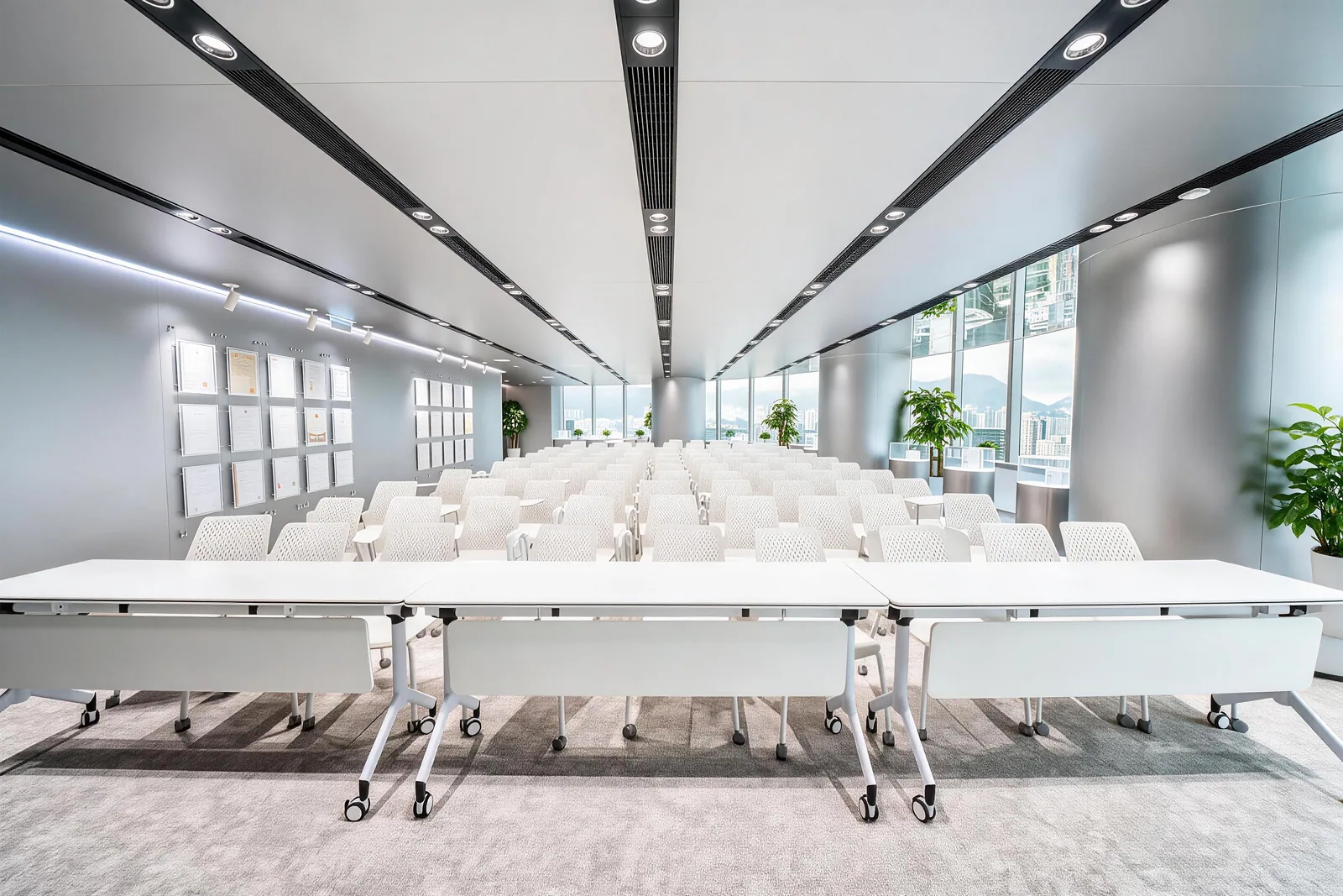 Rows of white chairs and tables facing the front of a long conference room, with windows along one side.