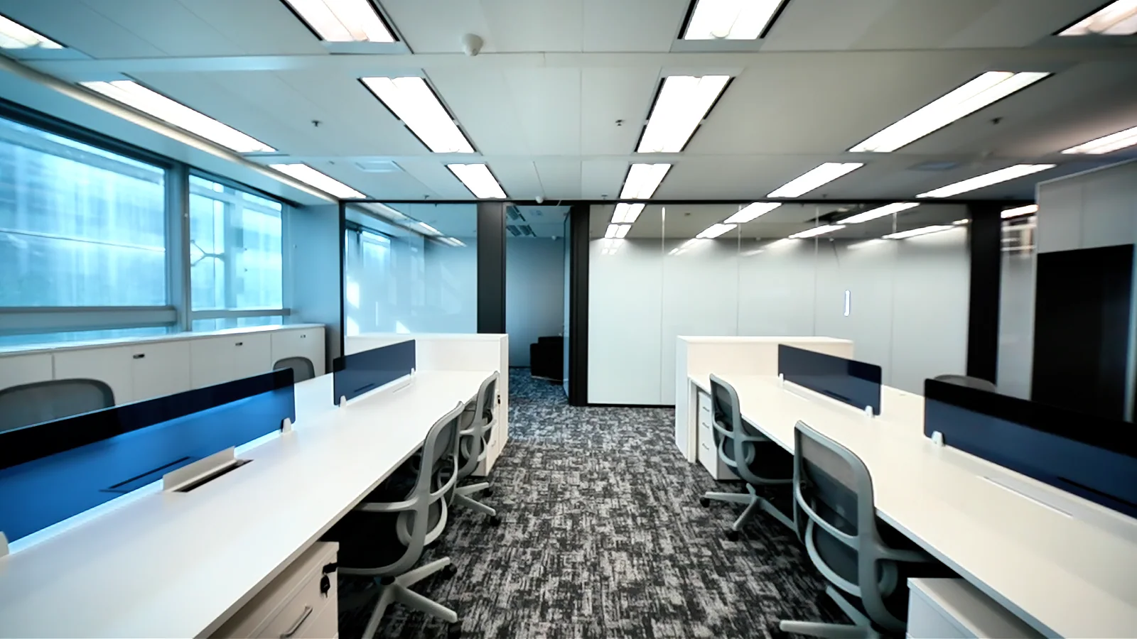 Completed office at Hong Kong Science Park, with white workstations, blue dividers and a glazed meeting room; still from the project film.