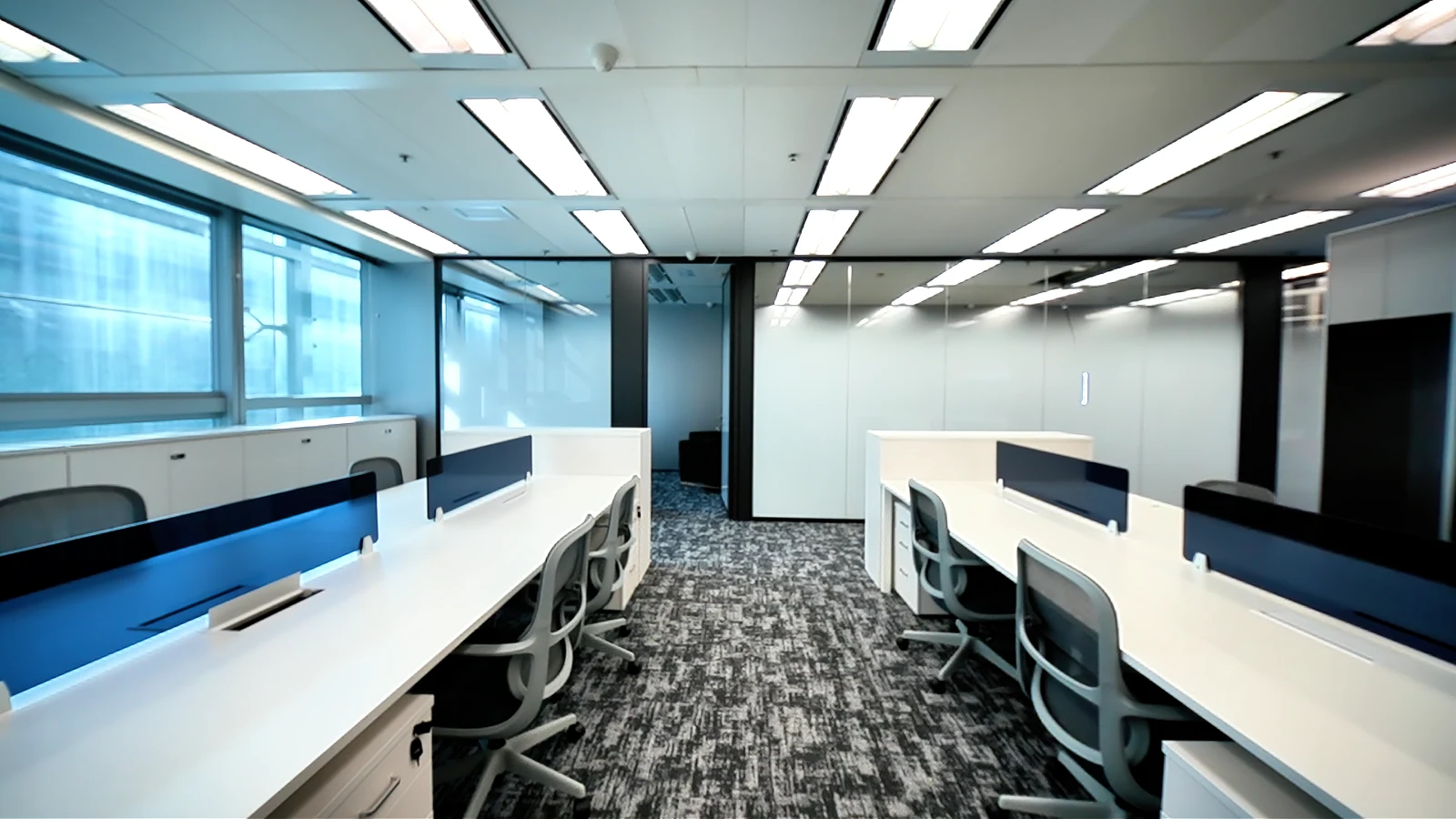 Completed Science Park office with white workstations, blue desk screens and a glazed meeting room.