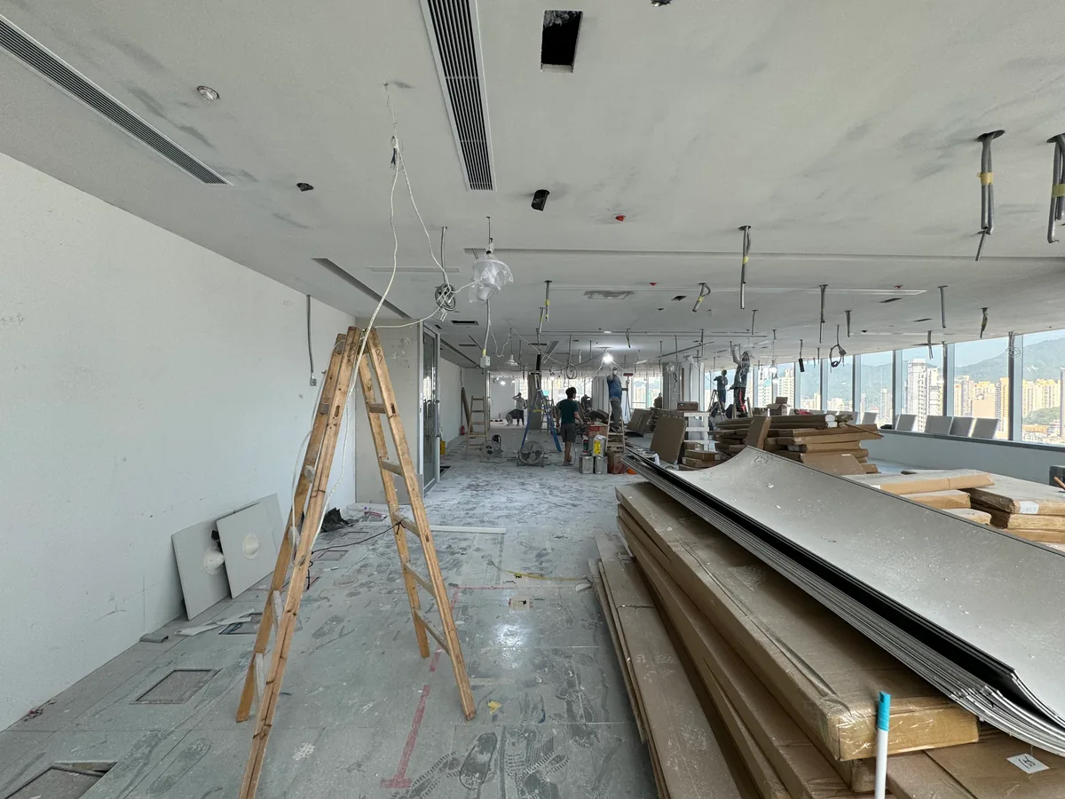 Unfinished window-side office area with exposed ceiling works, materials and fit-out activity.